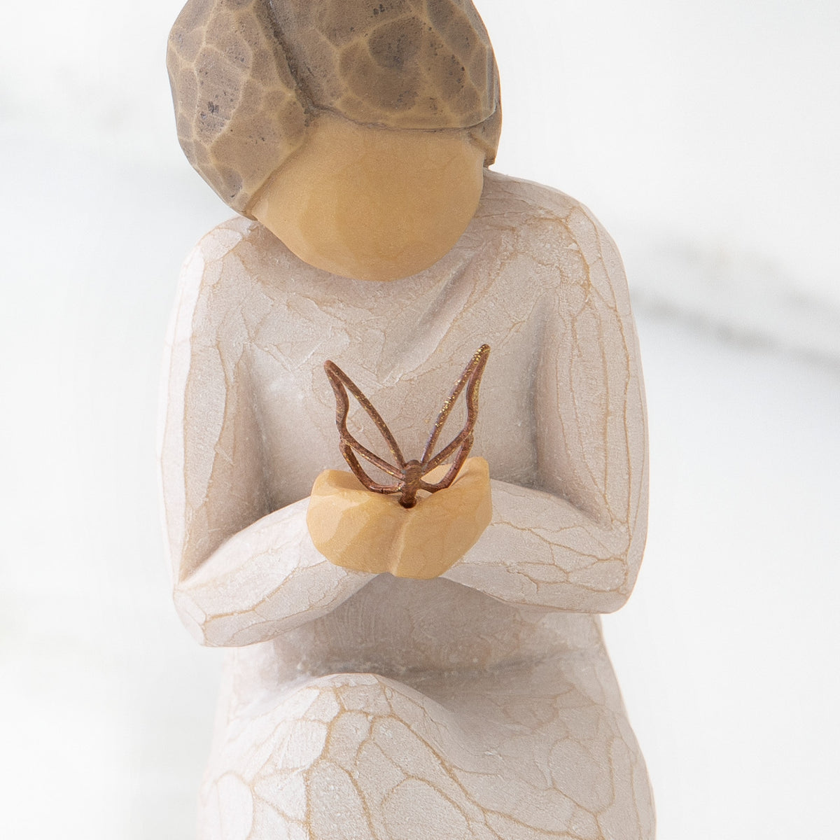 Close up of kneeling female figure in cream dress, holding wire butterfly on extended hands
