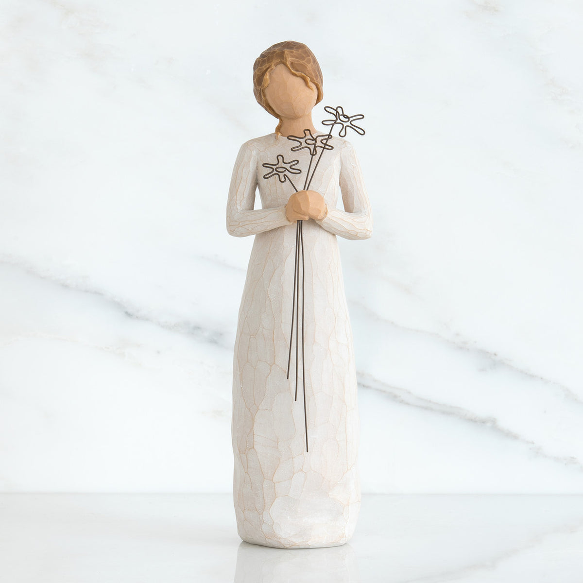 Front view of girl with brown hair in a bun holding three flowers with long stems up to her chest with both hands