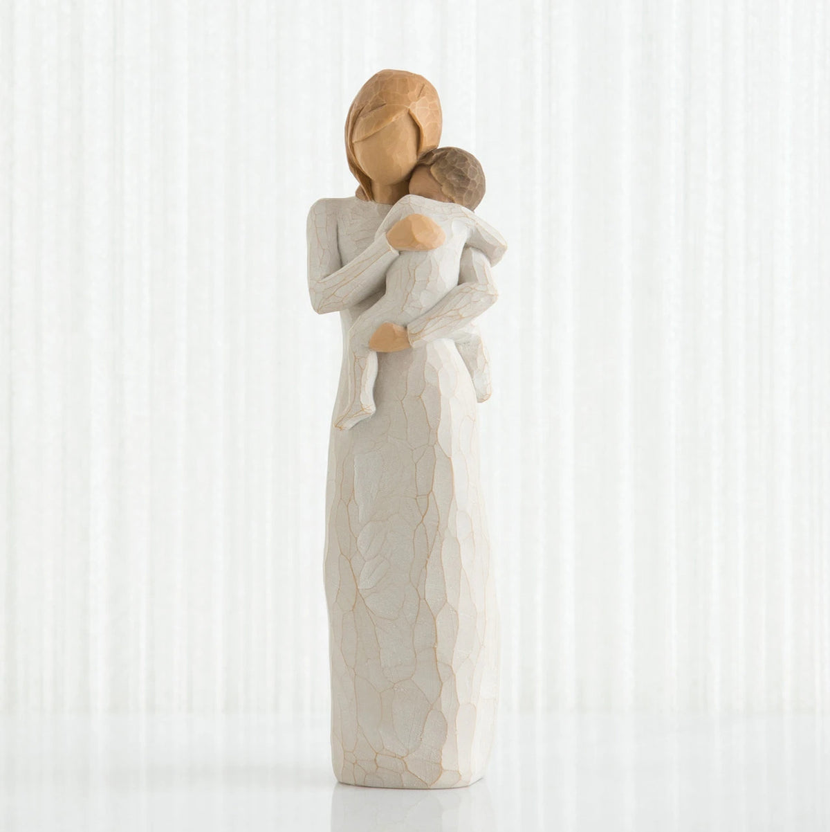 Faceless woman figurine in white dress holding brown haired baby in white clothes
