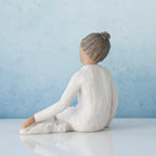 Small brunette girl figurine in white dress sitting away from the camera - blue background