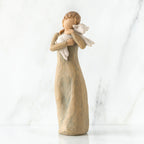 Faceless woman figurine standing wearing light tan dress holding white lamb in her arms