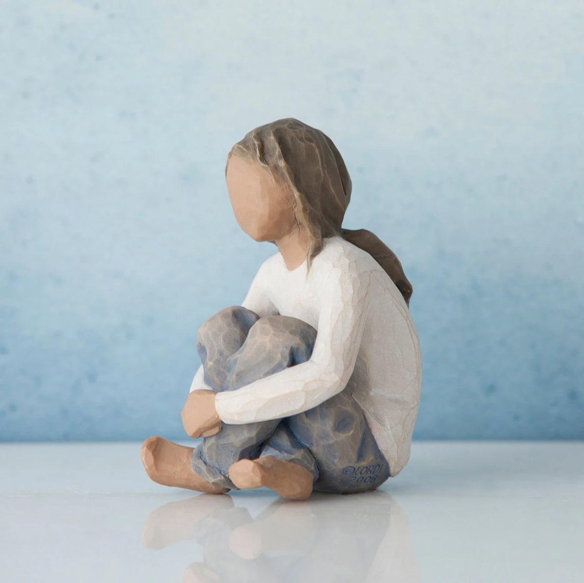 Brunette girl figurine sitting in white shirt and blue jeans with her arms folded on her legs - blue background