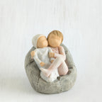 Two small baby figurines hugging another laying on grey beanbag