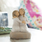 Willow Tree Sister mine, 4”h hand-painted resin figure of two girls in cream dresses, kneeling with arms around each other, on beside table