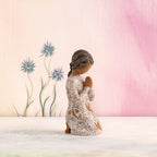 Willow Tree Prayer of Peace, 4”h hand-painted kneeling figure with darker skin and hair, in cream dress carved with nature imagery, in prayer/meditation pose, in front of pale pink painting