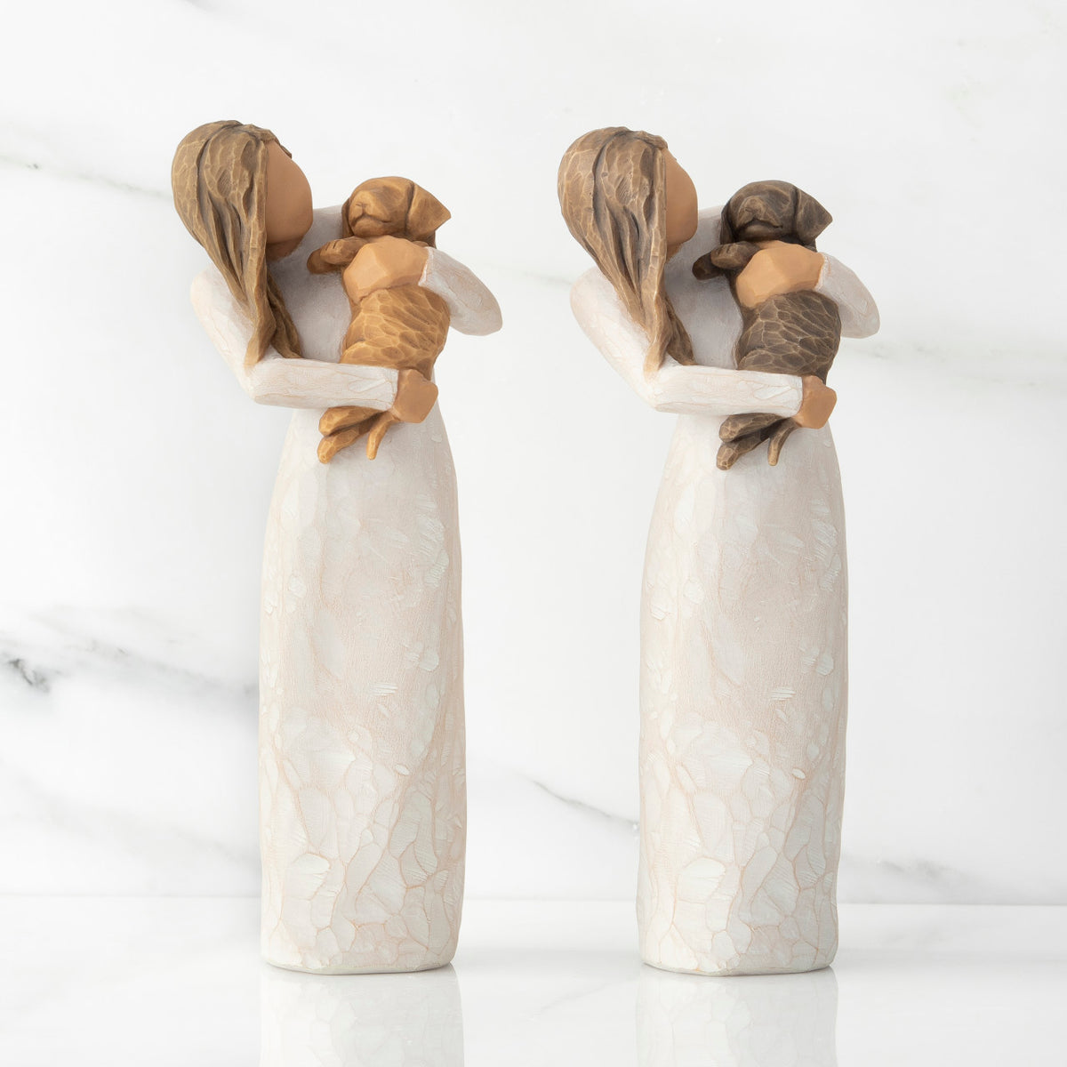 Front views of two standing female figures in cream dress, one holding dark color puppy, the other holding golden color puppy