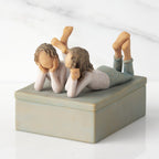 Left view of closed rectangular blue-gray resin box, sculpture of two girls affixed to lid